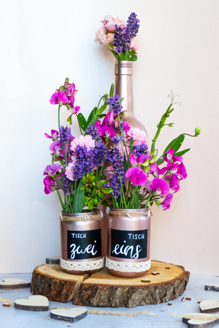 Zwei selbstbesprühte Blumenvasen in rose, welche dekoriert und mit einer schwarzen Tafelfolie beklebt wurde. Auf der Mitte der Vase ist die Folie mit weißem Stift belettert mit den Tischnummern.